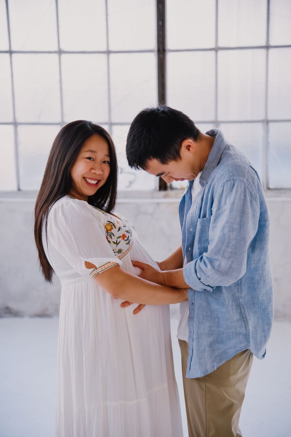 Playful maternity photos of couple in bright industrial space.
