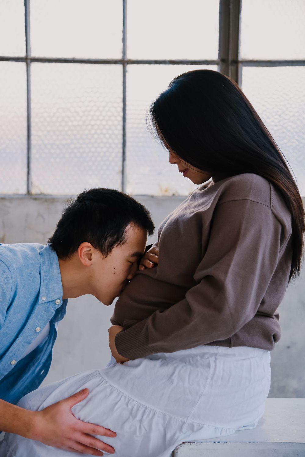 Couple in casual clothing sharing an intimate moment against a light background.