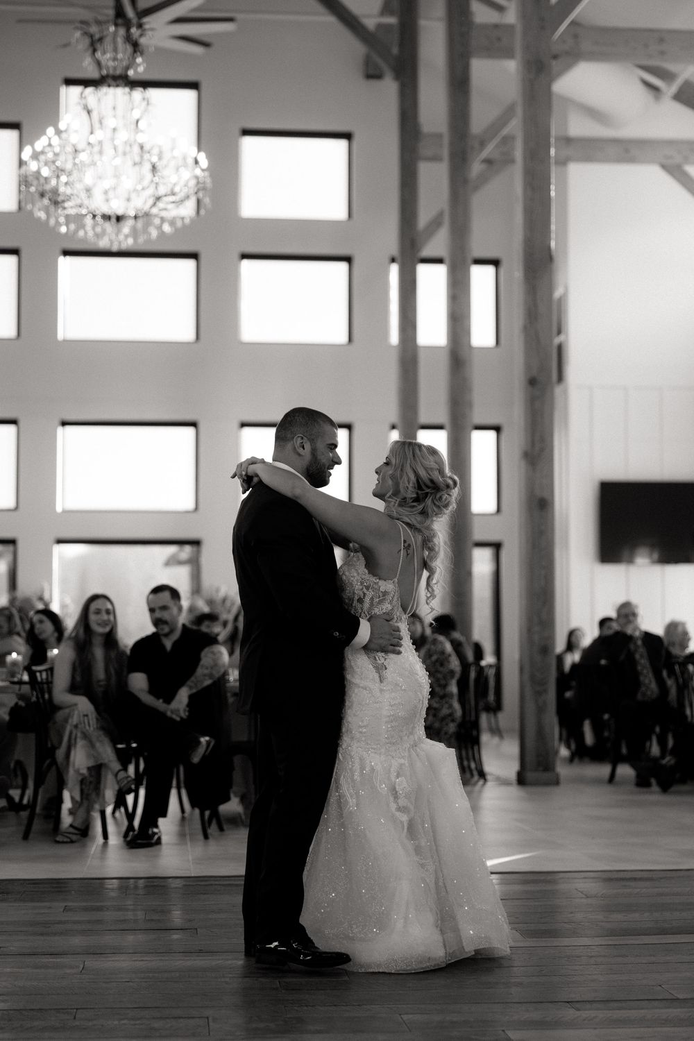 A couple shares their first dance at a wedding reception under a crystal chandelier in an elegant white venue.