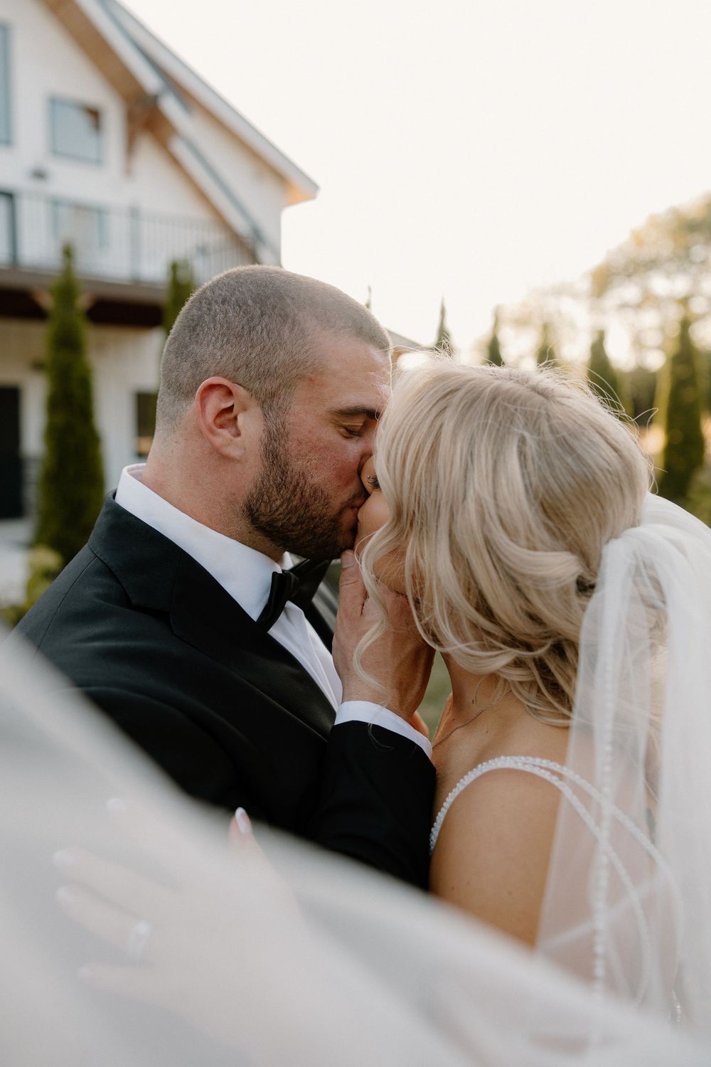 A romantic wedding couple shares an intimate kiss during golden hour at their outdoor ceremony.