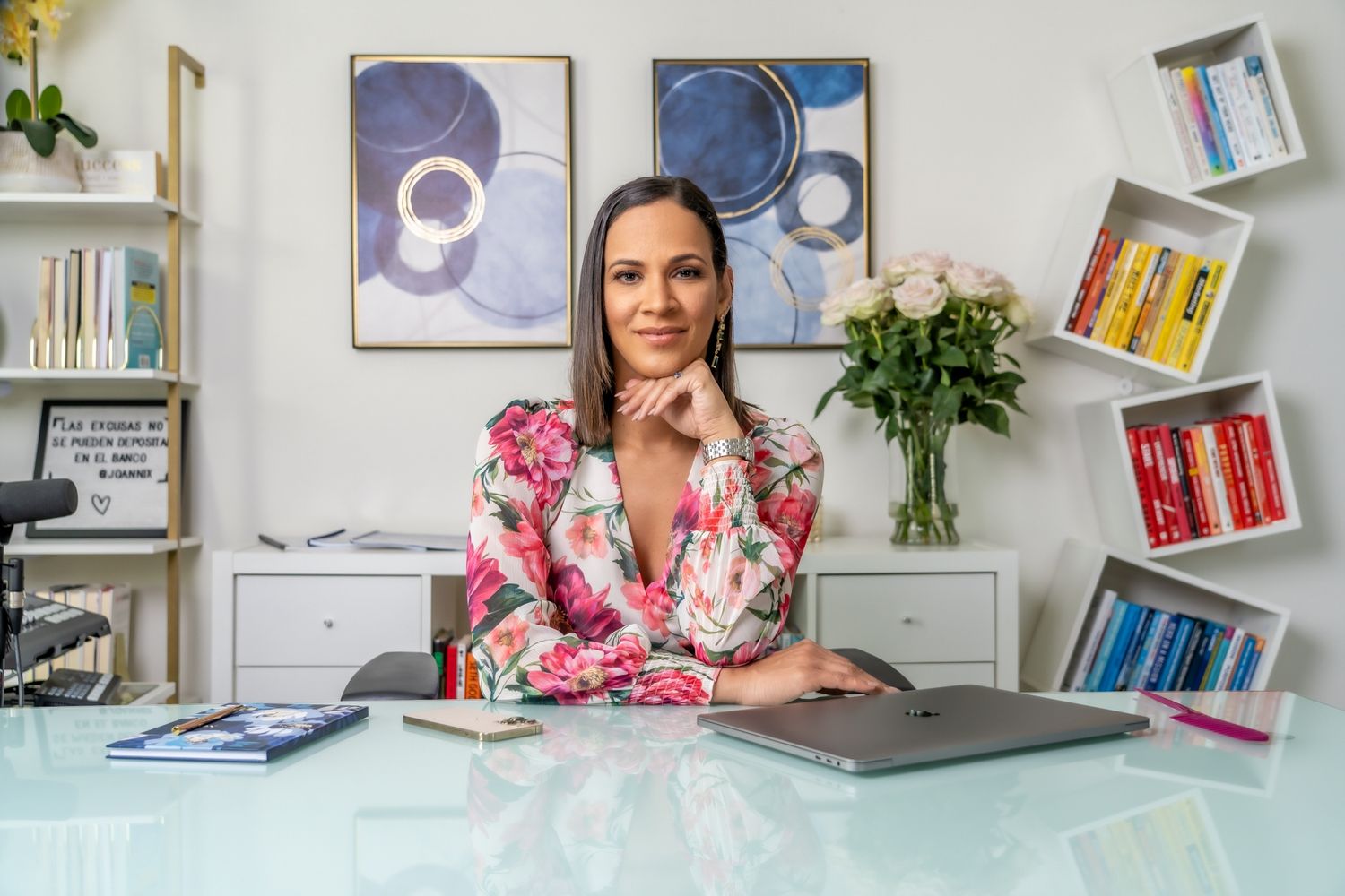 Business professional at modern desk with abstract art and bookshelf in background.