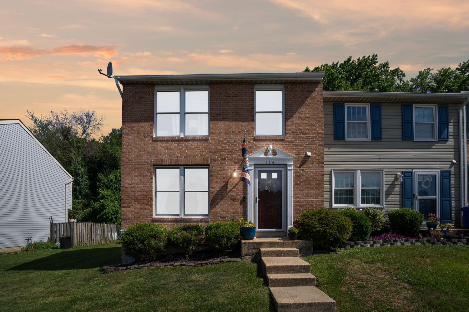 Modern brick townhouse with white trim and landscaping at sunset.