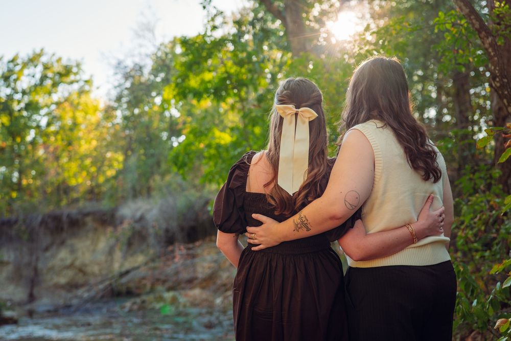Couple embraces against backdrop of trees during sunset.