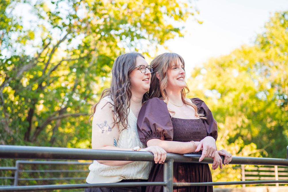 Couple shares affectionate moment in front of autumn trees and fence.