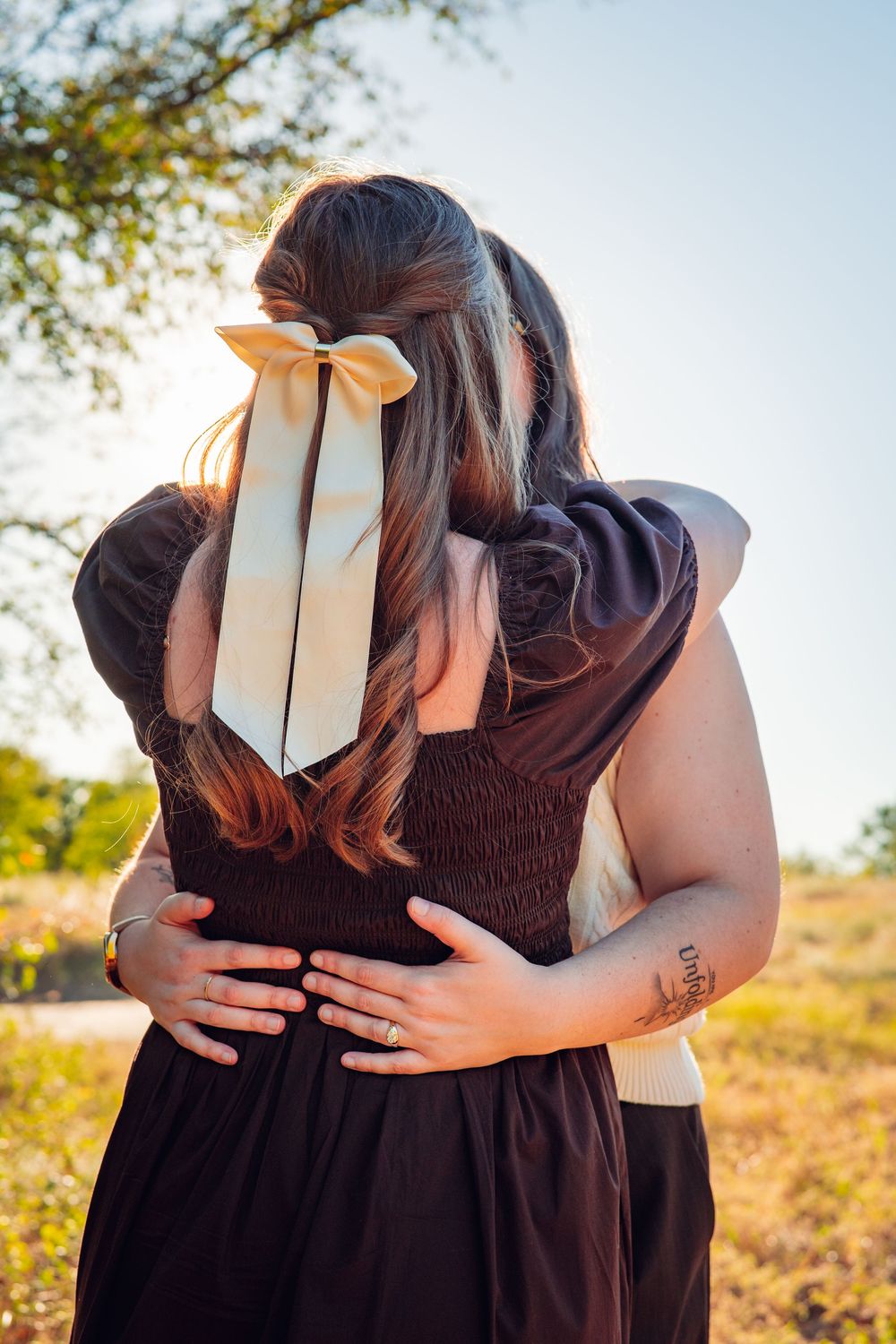 Close-up of two people embracing outdoors wearing brown and white outfits.