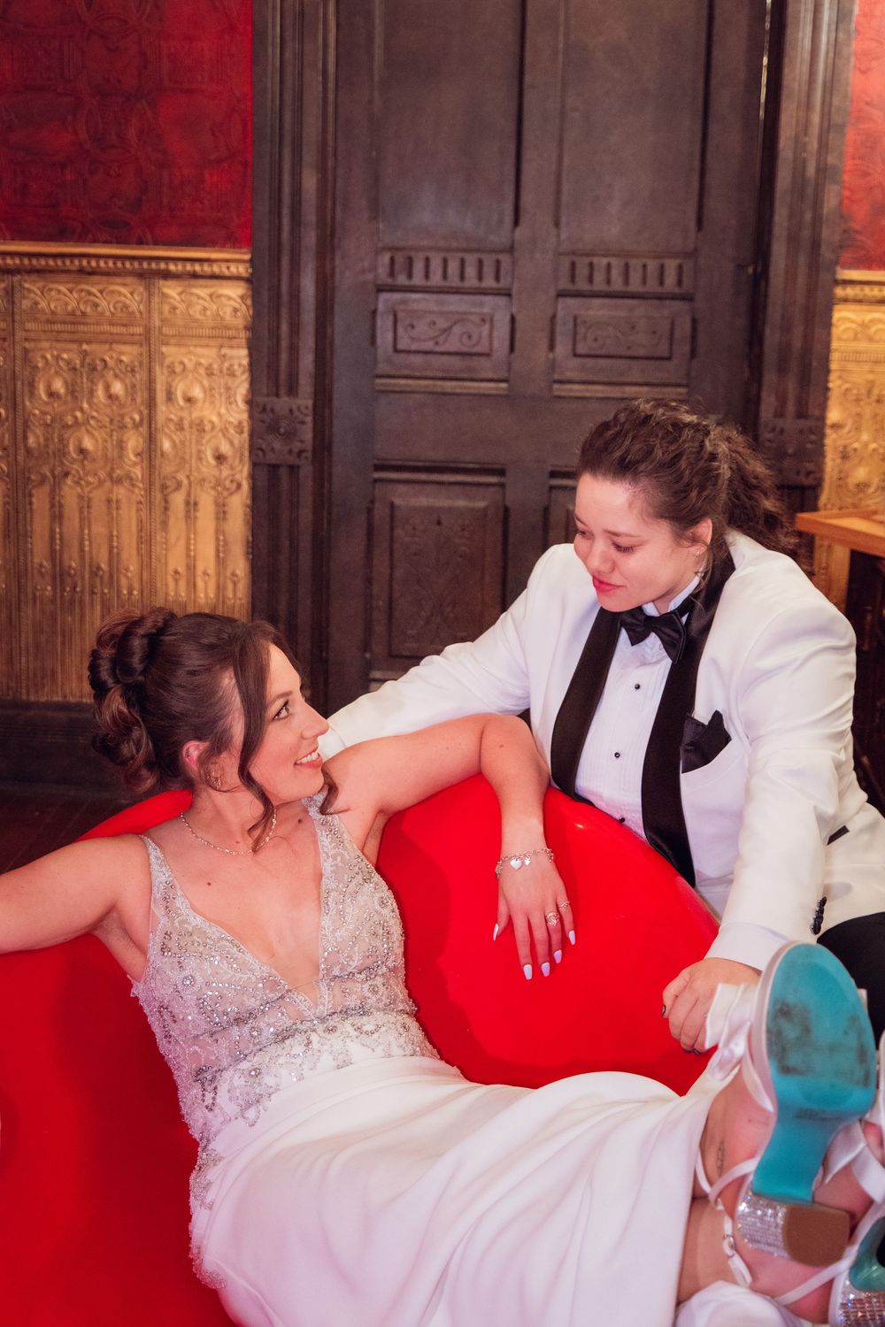 Couple in formal wear shares tender moments on a red couch.