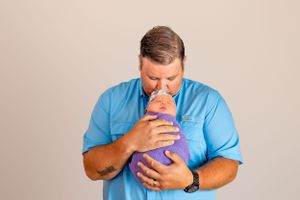 Person in blue shirt tenderly holding and kissing a baby wrapped in purple.