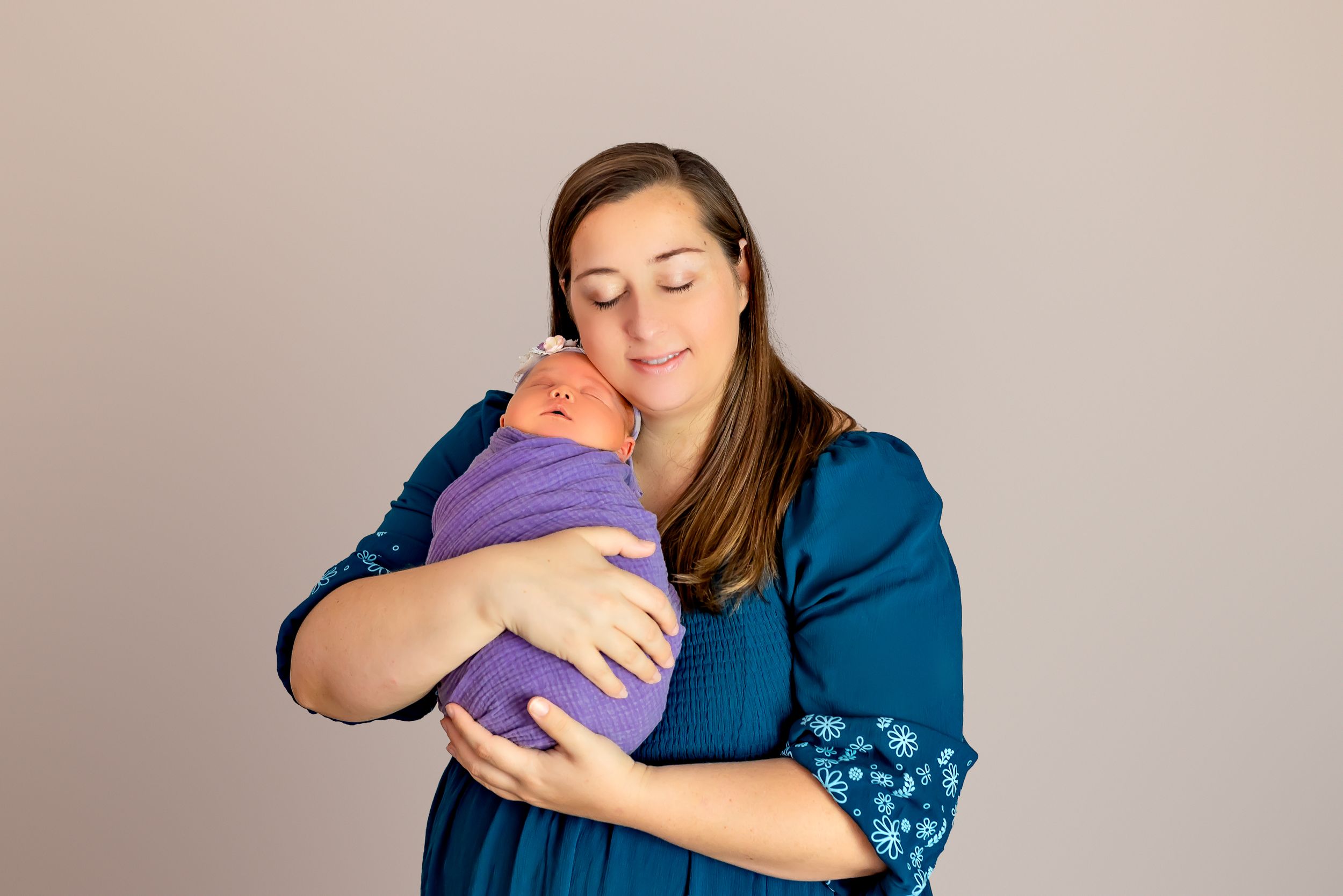Person in blue dress holding and embracing a baby swaddled in purple fabric.