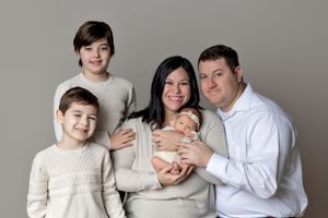 Family portrait with cream and white clothing against gray background.