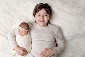 Portrait of two people in cream sweaters with baby on white backdrop.