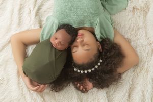 A series of four photos showing a baby lying on white bedding while wearing a sage green outfit.