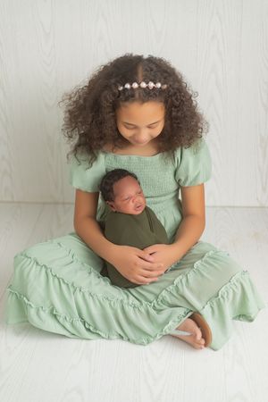 A series of tender moments showing a parent in mint green dress cradling a sleeping newborn against white backdrop.