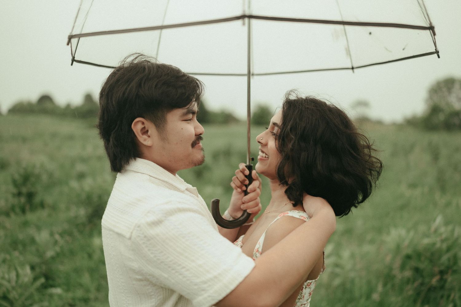 A playful engagement photo of a couple laughing together in a wooded setting at sunset.