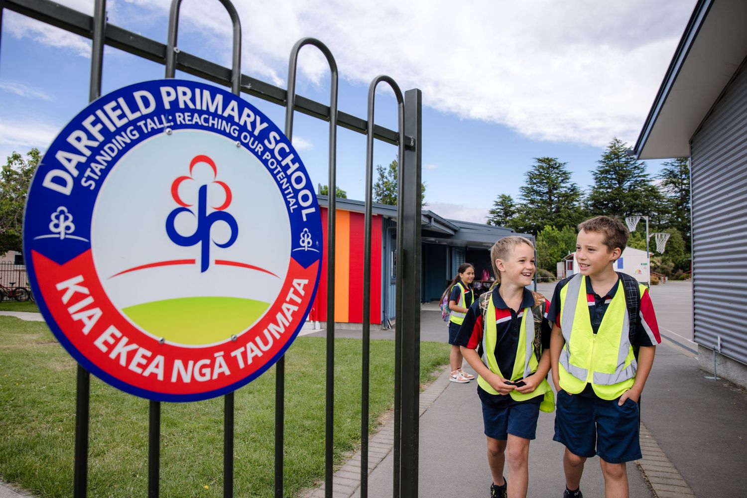 Students in safety vests walk past Danield Primary School sign.