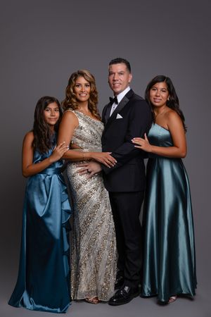 A formal group portrait of four people wearing elegant evening attire including blue gowns and a sequined silver dress.