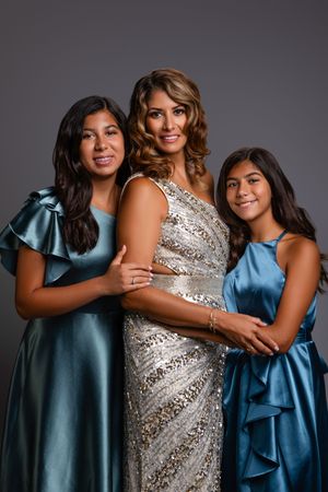 Three people in evening gowns pose together, wearing blue satin and sequined dresses for a formal portrait.