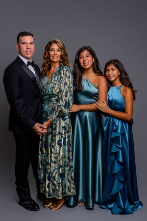 A family of four poses for a formal portrait against a dark background wearing elegant blue evening attire.