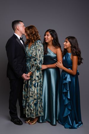 A formal family portrait shows group of four people in elegant attire against dark grey background.