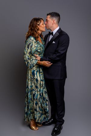 A couple in formal attire share intimate moments while dancing in a studio with dark grey background.