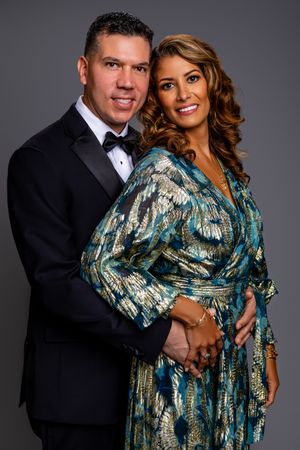 Couple poses for formal portrait series with woman in shimmery teal and gold dress and man in classic black tuxedo.