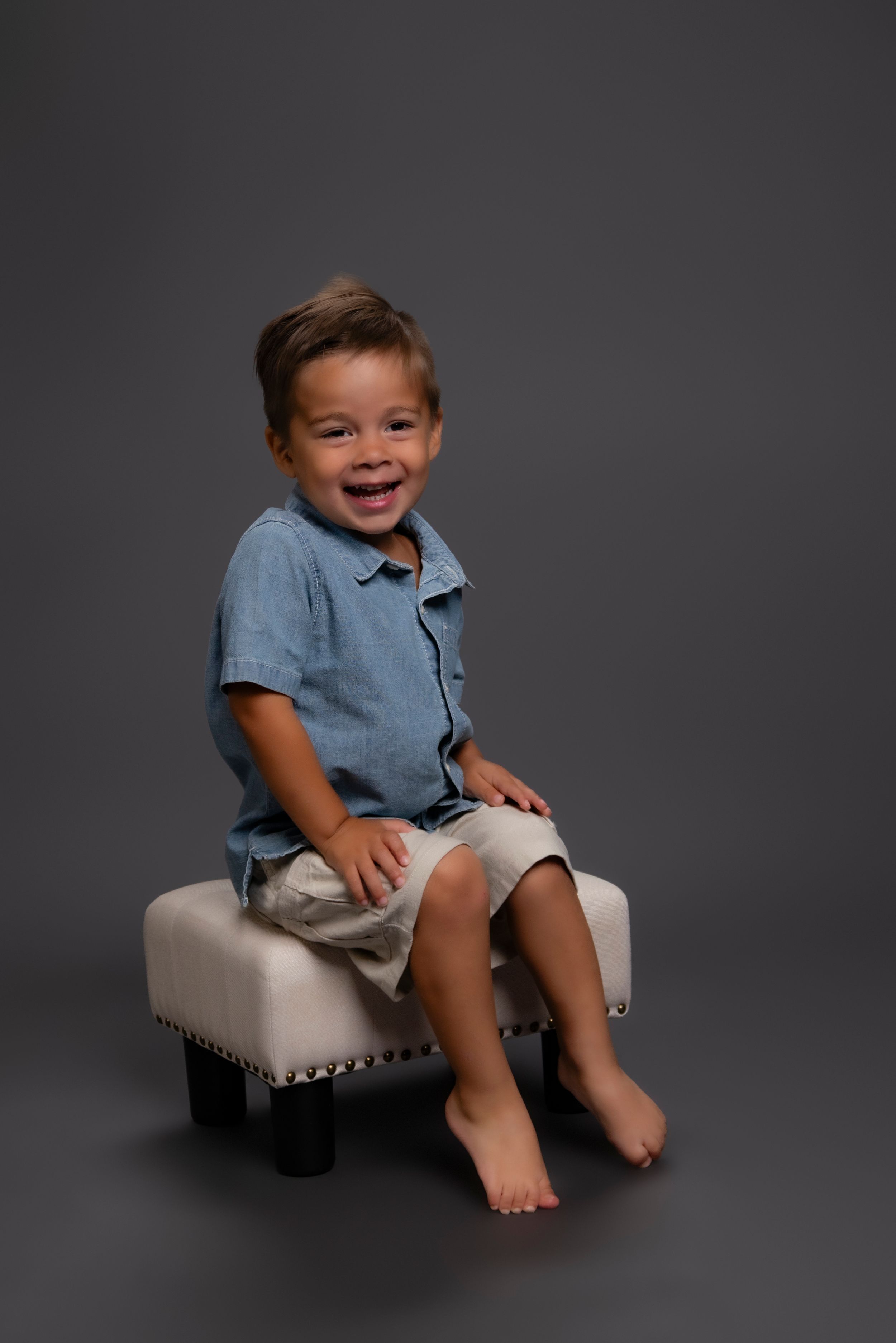 Sequence of photos showing a small child in a blue shirt sitting on a cream-colored ottoman against a dark gray backdrop.