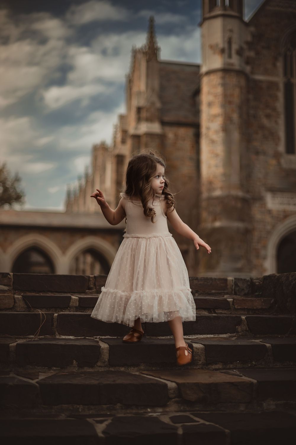 Girl wearing a light tulle dress creates dreamy silhouette against gothic cathedral architecture at sunset.