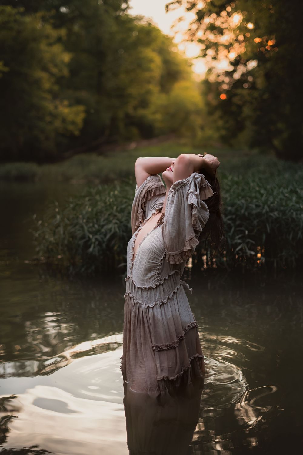 A woman poses in a creek and shakes out wet hair.