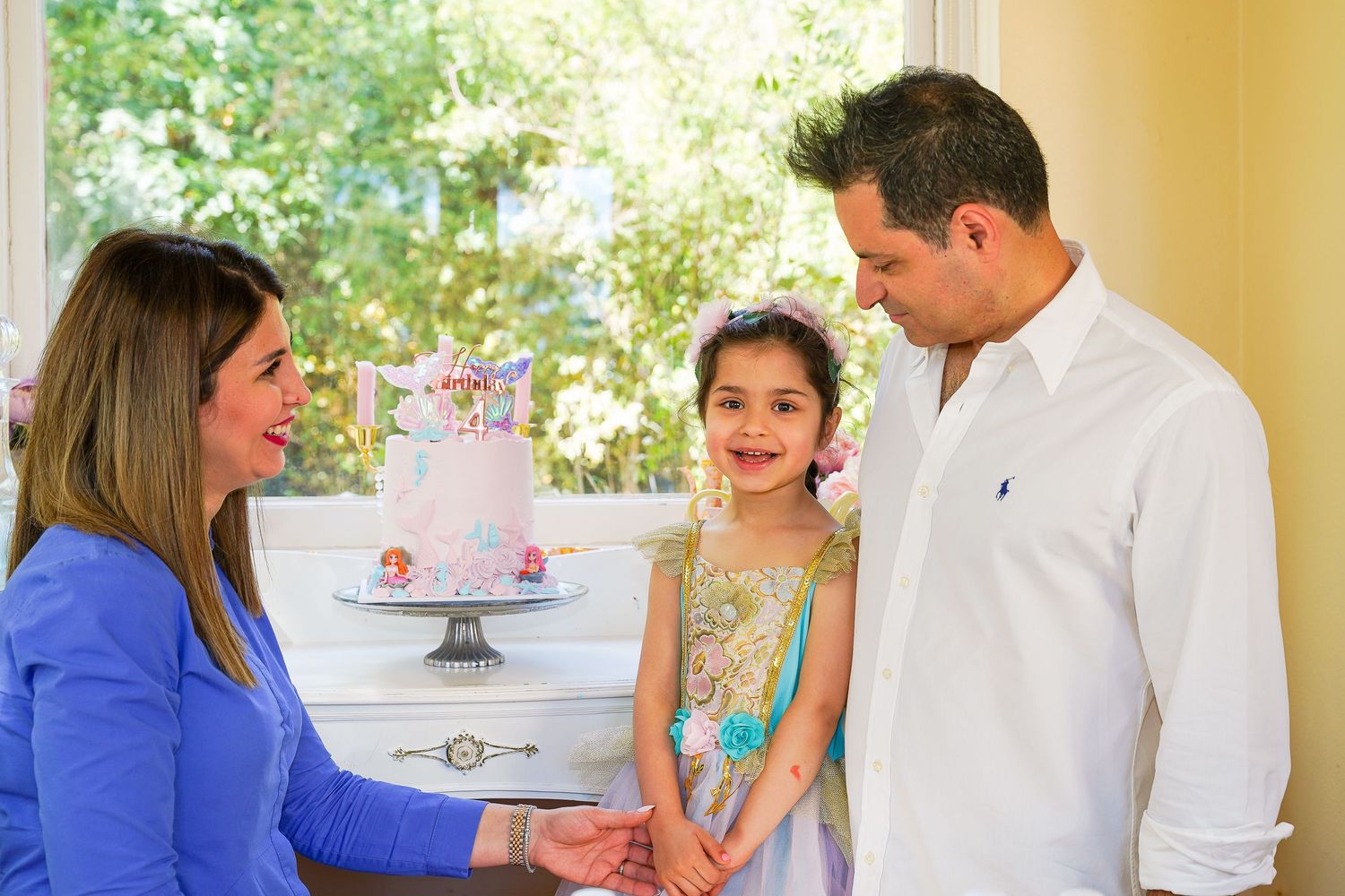 Family celebrating young girls birthday with a floral cake at an outdoor garden party.