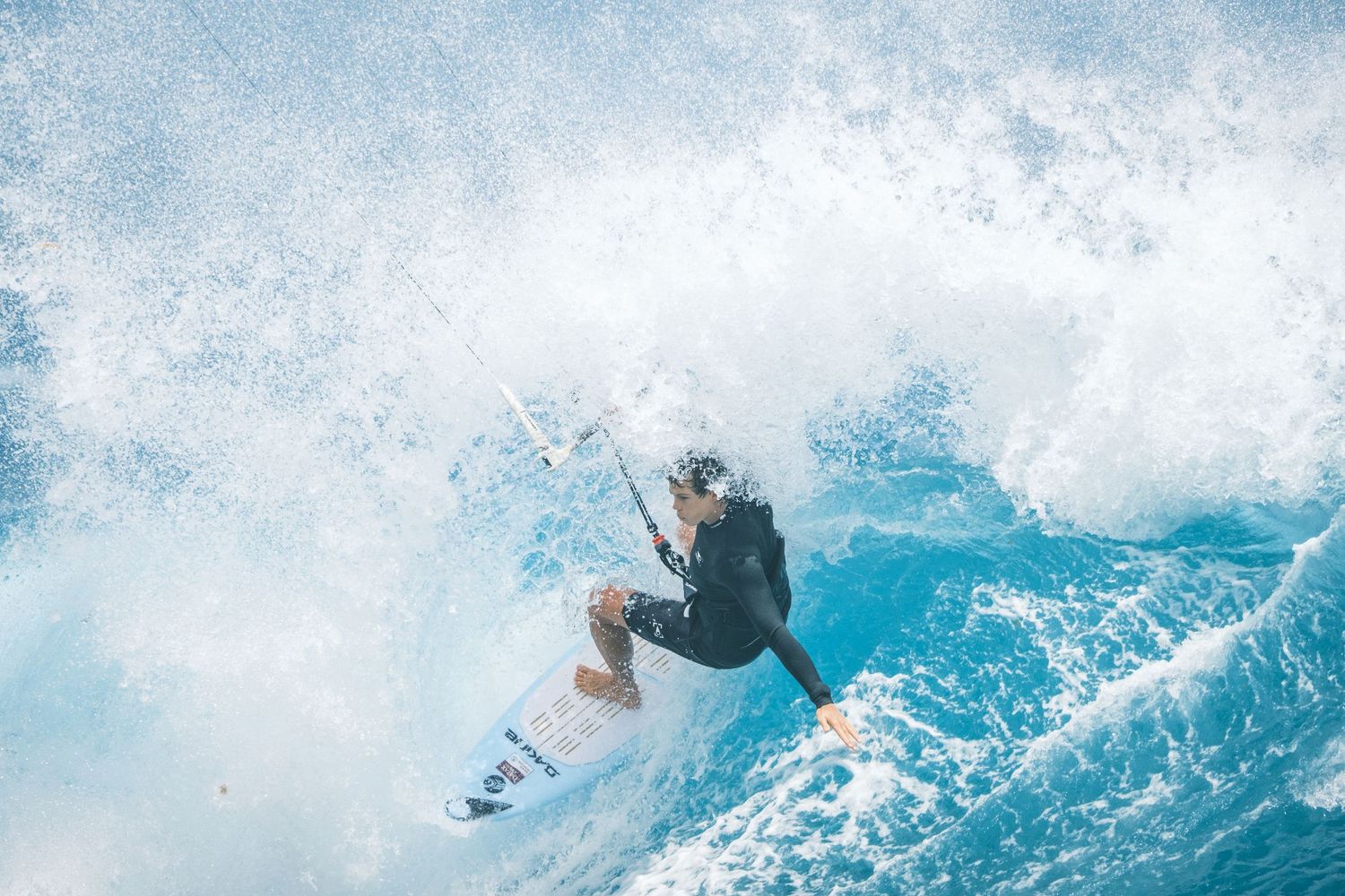 Surfer carves through a massive blue wave with dramatic ocean spray in the background.