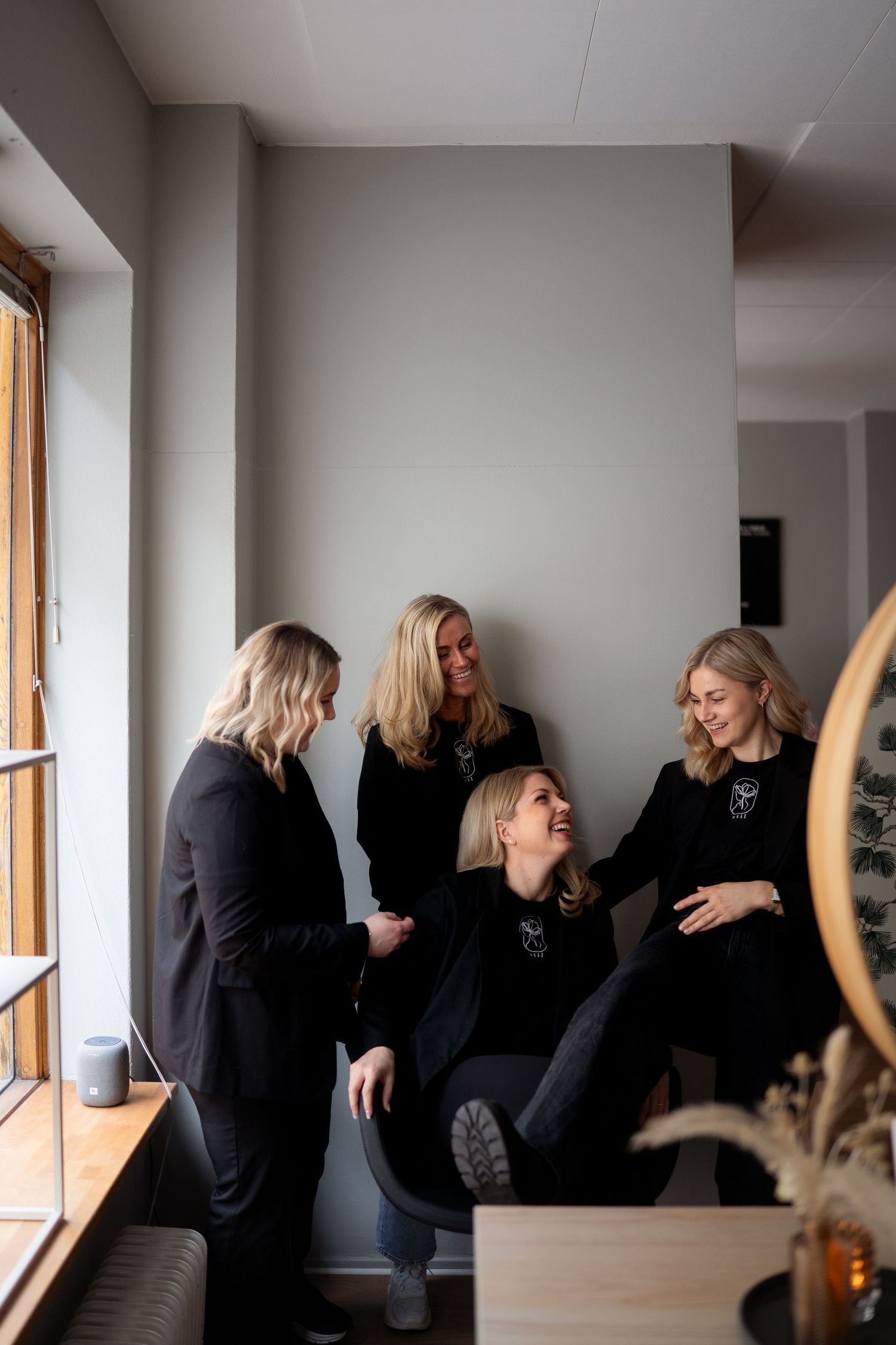 A group in black clothing shares a lighthearted moment together while gathered near a window in an interior space.