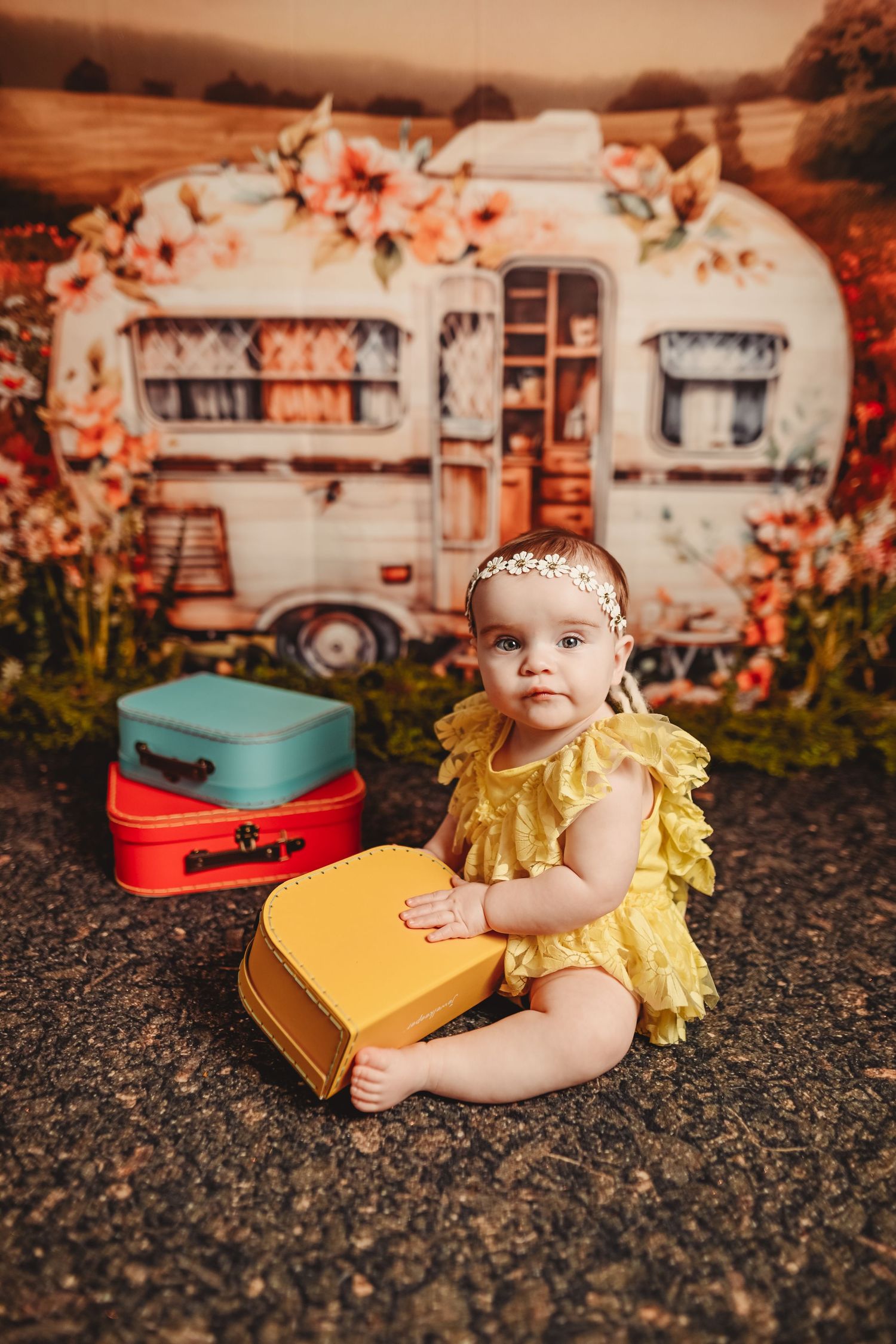 Vintage travel themed baby portrait with yellow suitcase and retro camper background.