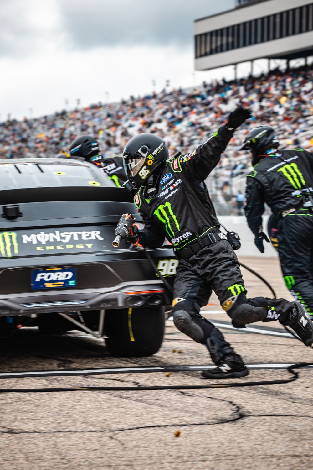 Pit crew members in black uniforms service a race car during a high-speed pit stop.