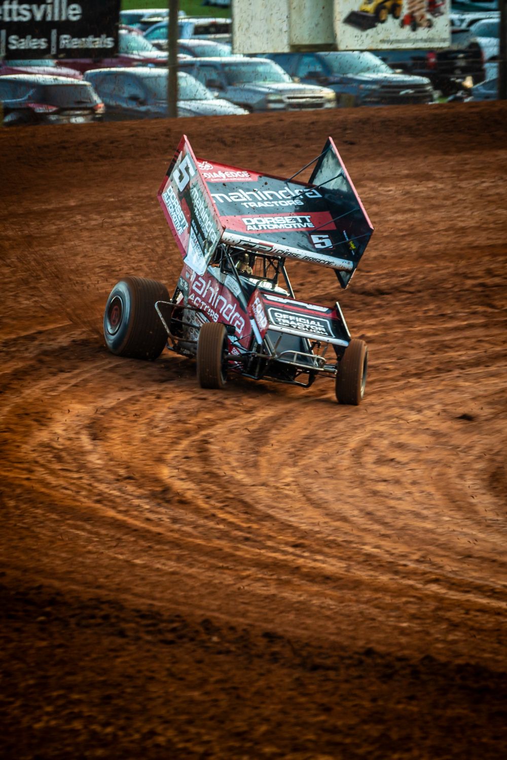 Sprint cars racing on a dirt track leaving trails of dust behind them.
