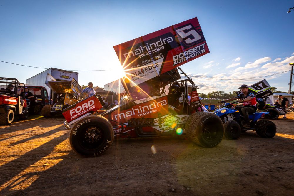 Racing vehicles silhouetted against dramatic sunset sky at outdoor track.