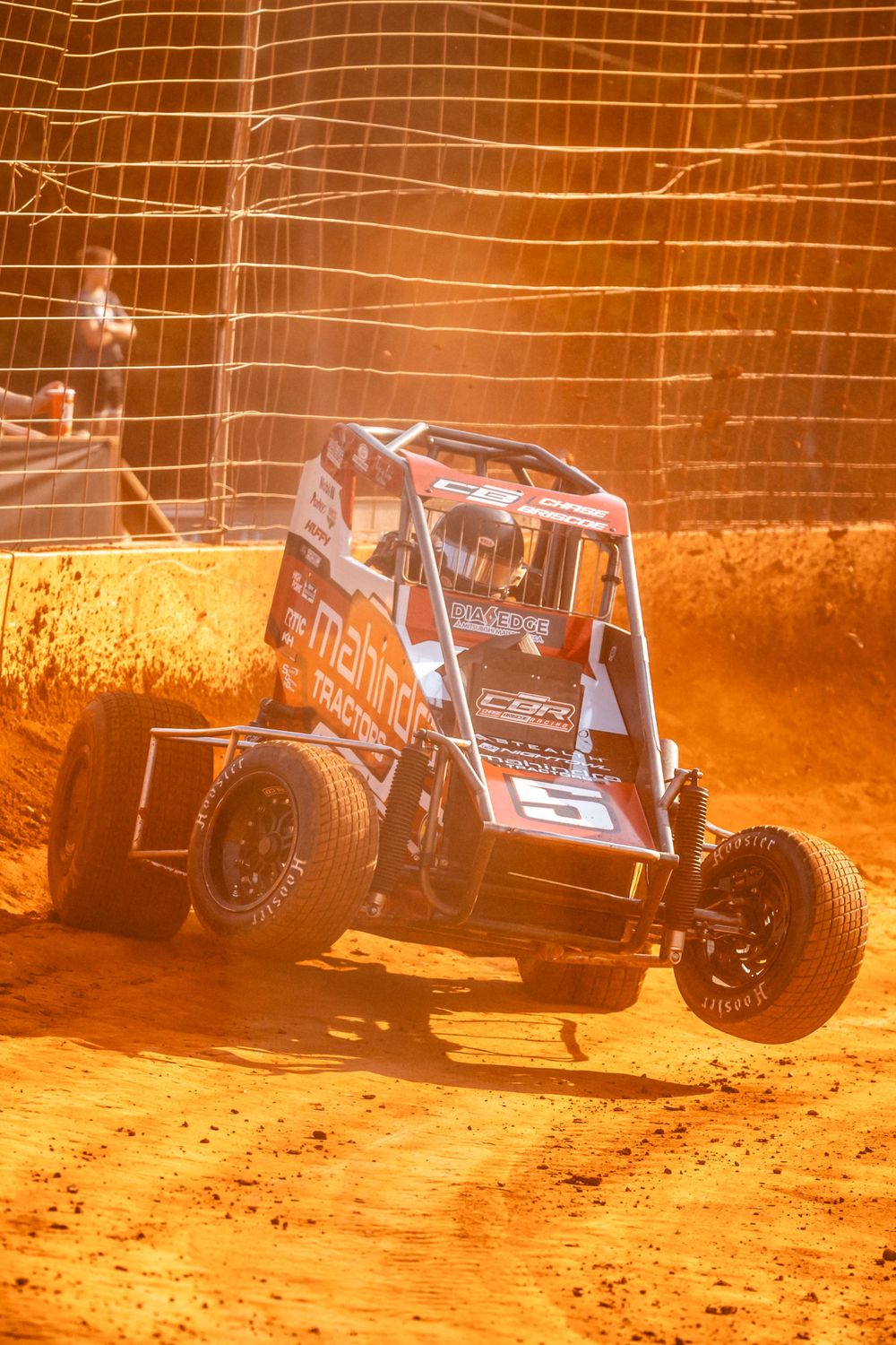 Off-road racing vehicles kicking up orange dirt as they navigate a dusty track.