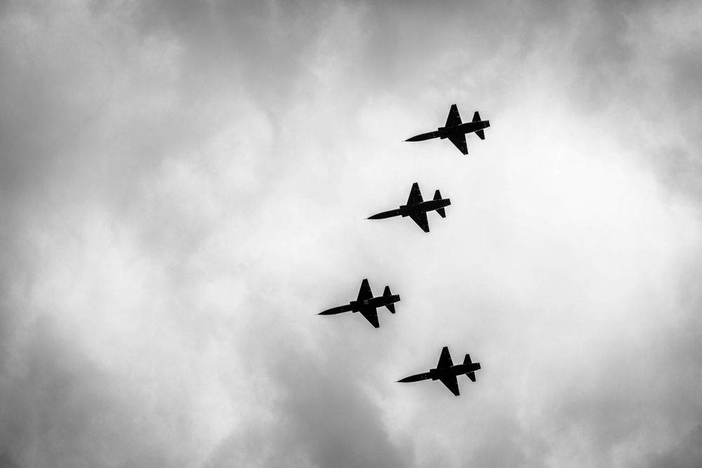Military fighter jets performing a formation flyover against cloudy skies.