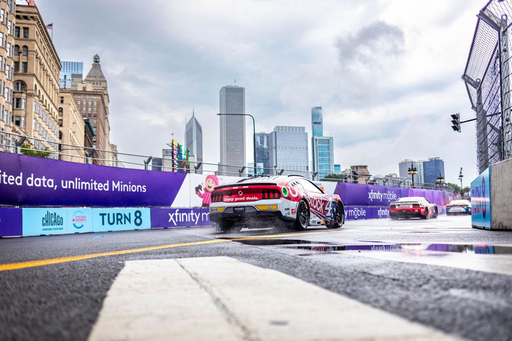 Urban racetrack with city skyline visible in background under cloudy skies.