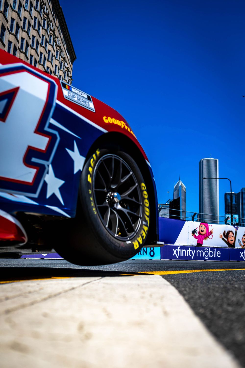 Low angle view of NASCAR race car tire against bright blue sky with advertising barriers.