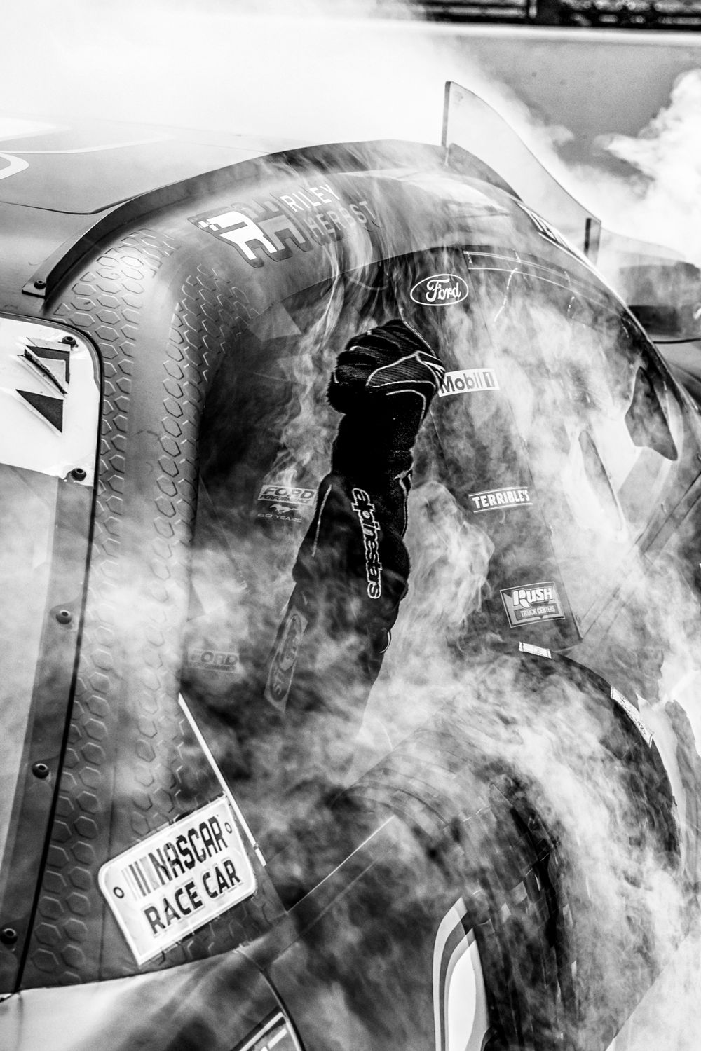 Smoke billows around NASCAR race cars at Indianapolis Motor Speedway.