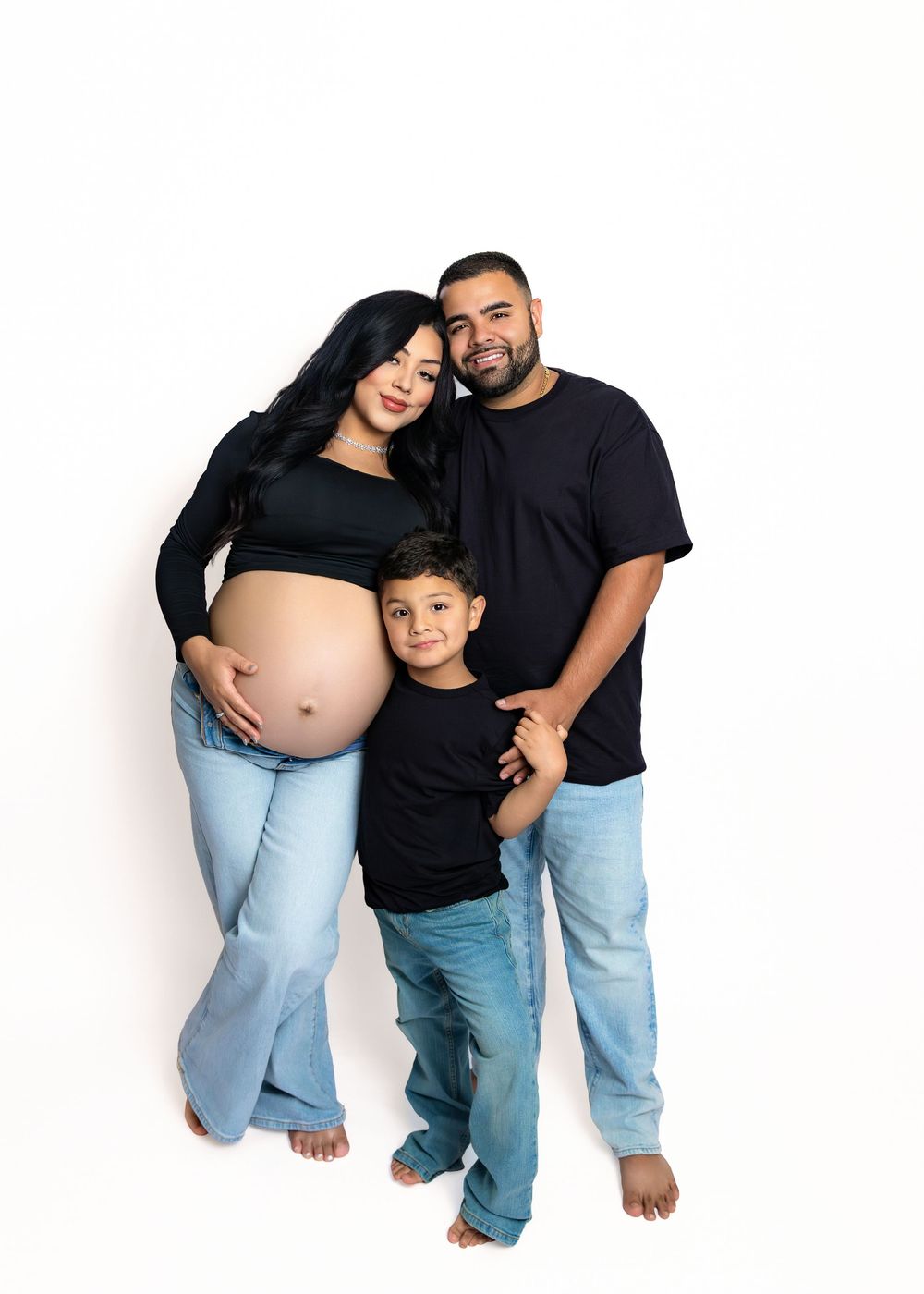 A pregnant woman, her partner and young child pose together in matching light blue pants for a series of maternity photos.