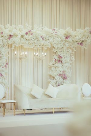 Elegant white and pink floral arch backdrop with modern white seating for wedding ceremony.