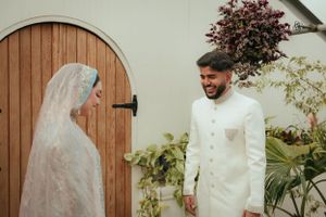Couple sharing a joyful moment in traditional wedding attire near wooden door with greenery.