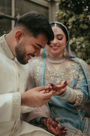 Wedding couple in traditional attire share intimate moment during mehndi ceremony.