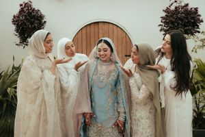 Wedding celebration with group in white traditional attire sharing joyful moment in greenhouse.