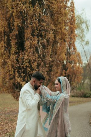 A couple in traditional wedding attire sharing a romantic moment among autumn trees.