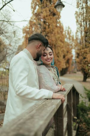 Romantic autumn wedding portrait showing couple in white traditional attire by wooden railing.