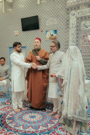 A wedding ceremony takes place on an ornate carpet in a mosque with traditional decorations.