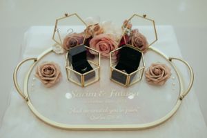 Wedding ring boxes surrounded by dusty pink roses and gold geometric decor on white surface.