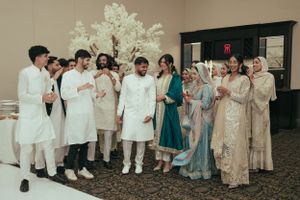 Wedding party dressed in elegant white and pastel traditional South Asian attire pose together indoors.