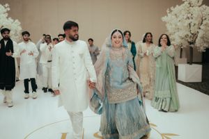 Traditional South Asian wedding ceremony with couple in white and blue attire walking on stage.